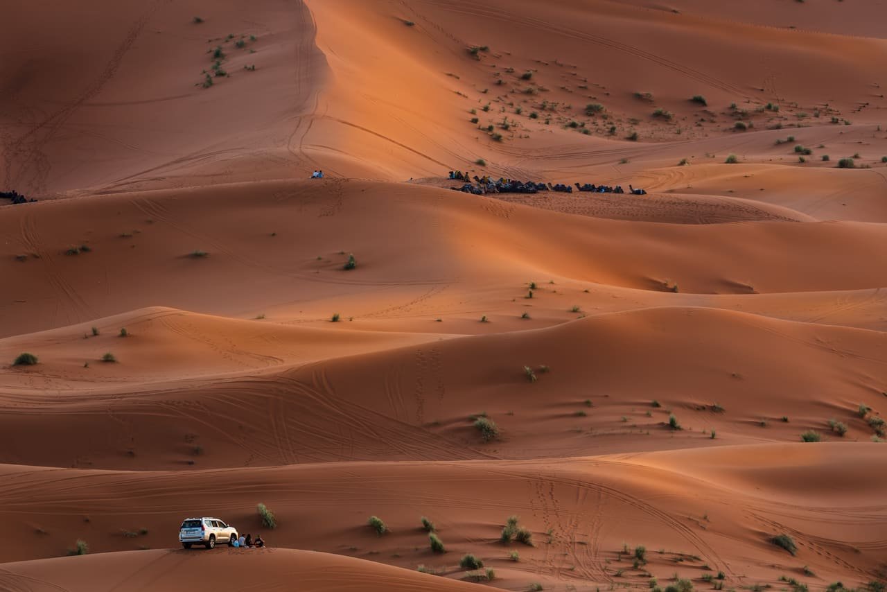 Des voyageurs regardent le soleil se coucher sur les dunes du Sahara marocain